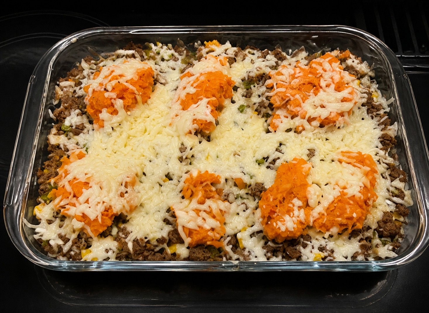 Cottage pie casserole with ground beef, mixed vegetables, mashed sweet potato, and melted cheese in a glass baking dish.