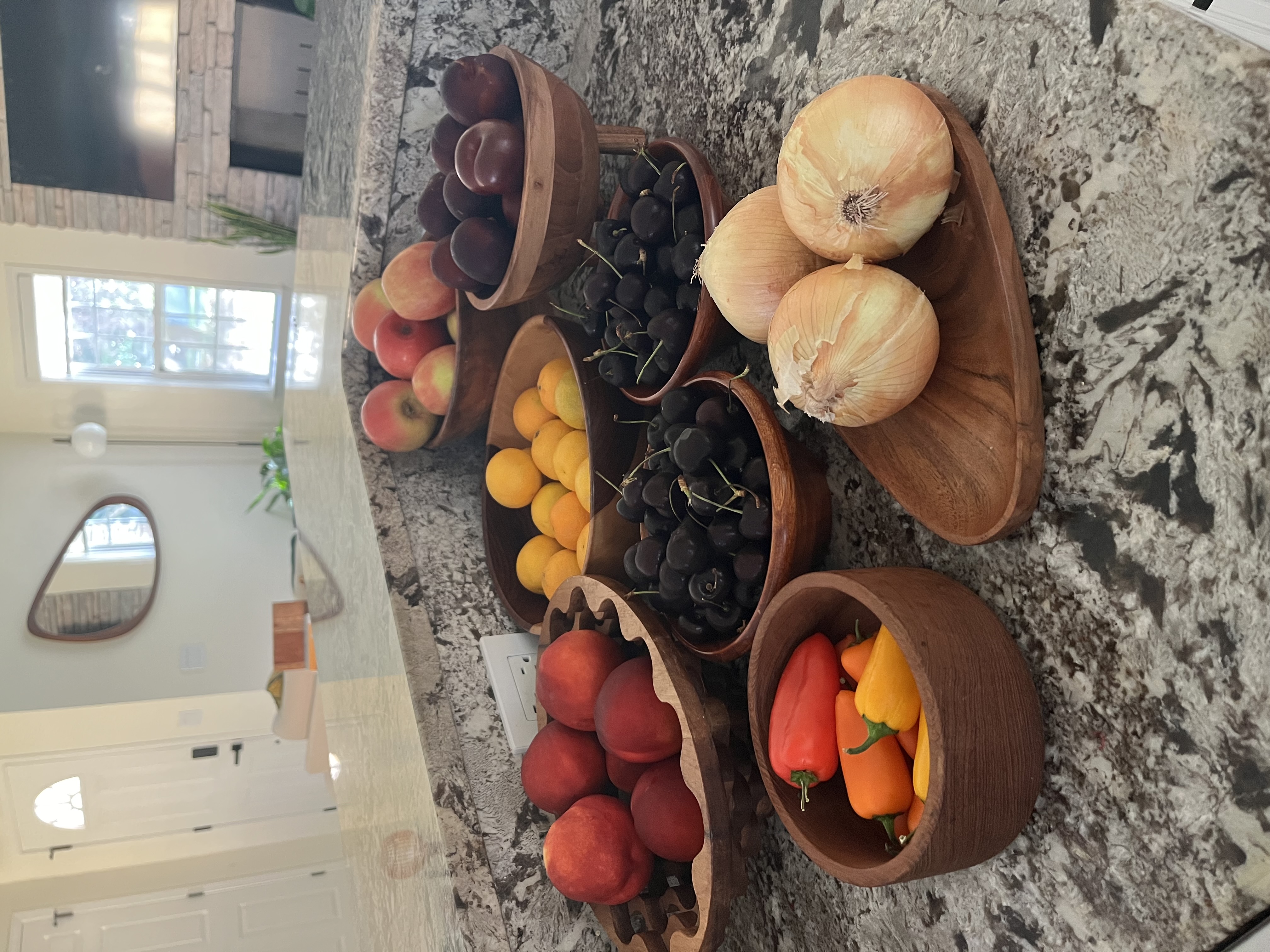 Assorted fresh fruits and vegetables arranged in wooden bowls on a kitchen counter.