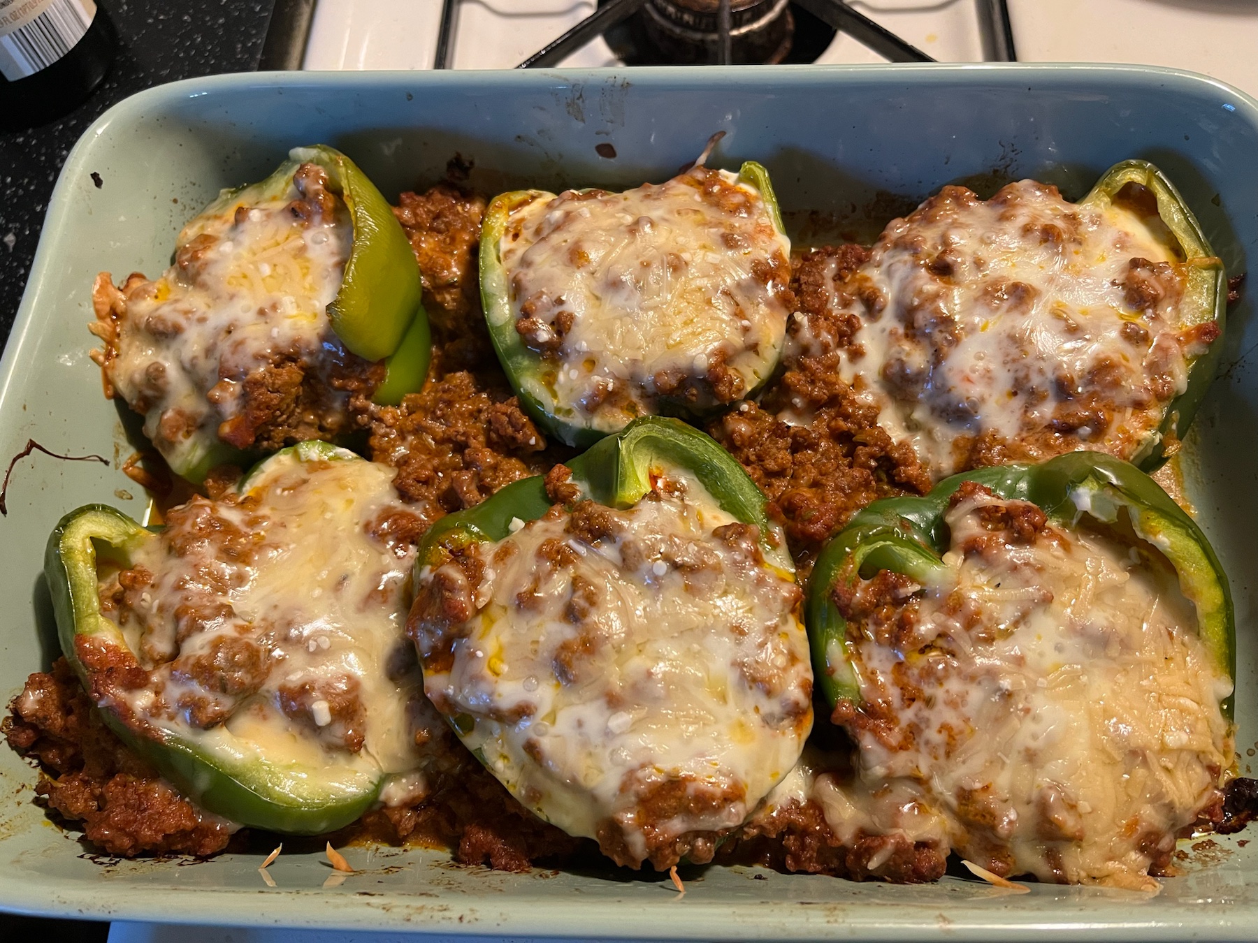 Stuffed green bell peppers topped with melted cheese in a baking dish.