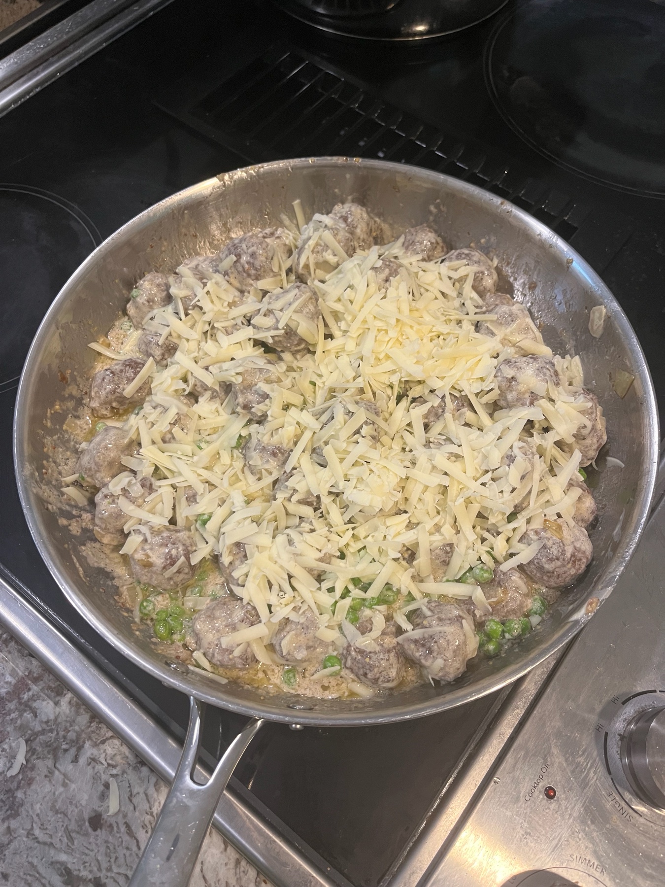 Swedish-inspired meatballs with peas and shredded cheese in a creamy sauce.