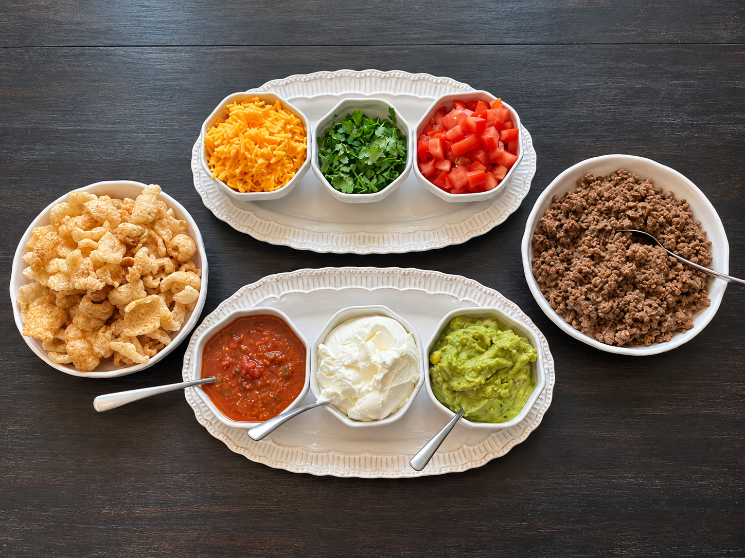 Taco bowl spread with seasoned ground beef, cheese, tomatoes, cilantro, salsa, sour cream, guacamole, and pork rinds.