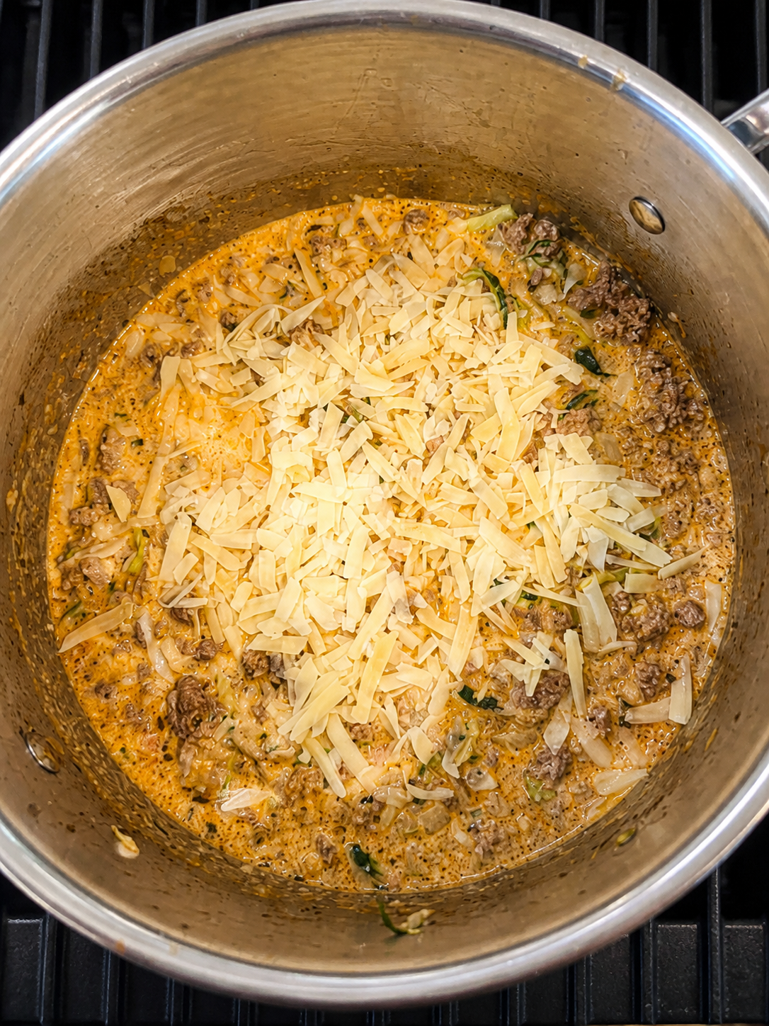 Creamy zucchini Bolognese with ground beef and grated cheese in a stainless-steel pot.