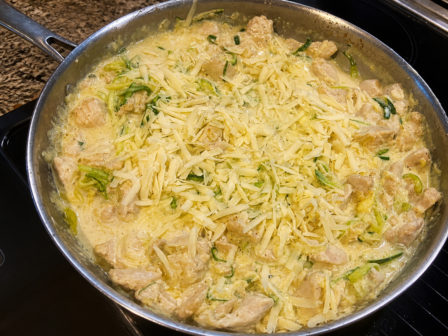 Zucchini chicken Alfredo with shredded cheese in a stainless-steel skillet.